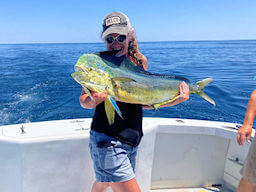 Pretty young lady angler holds up with enthusiasm a really big colorful mahi she caught on her offshore trip.